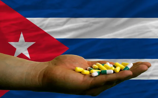 Holding pills in hand in front of cuba national flag — Stock Photo, Image