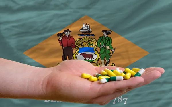 Holding pills in hand in front of delaware us state flag — Stock Photo, Image