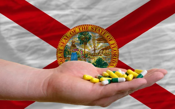 Sosteniendo pastillas en la mano delante de Florida nos bandera del estado — Foto de Stock