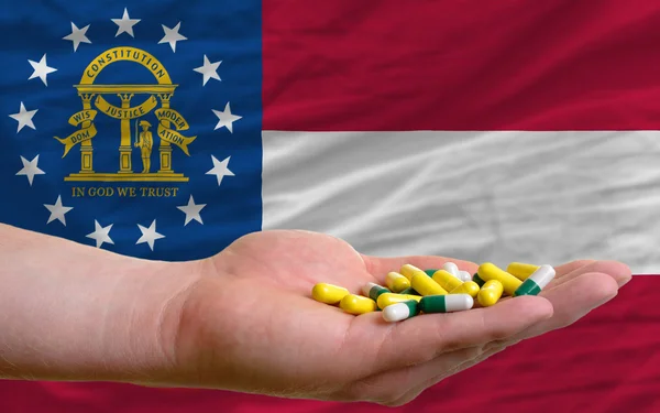 Holding pills in hand in front of georgia us state flag — Stock Photo, Image