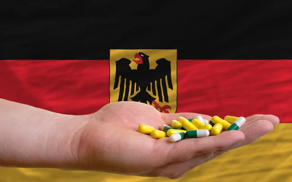 Sosteniendo pastillas en la mano frente a la bandera nacional de Alemania — Foto de Stock