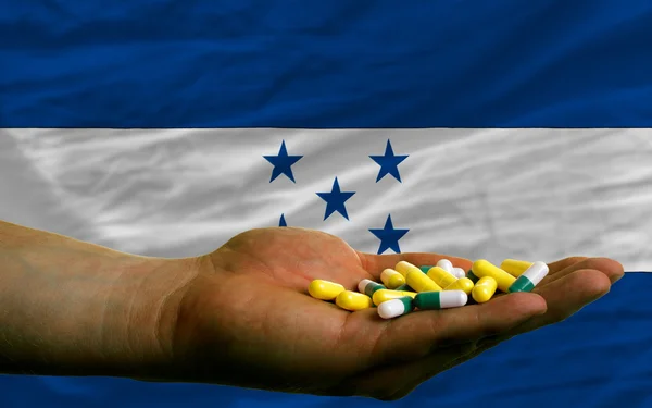 Tenendo le pillole in mano davanti alla bandiera nazionale honduregna — Foto Stock