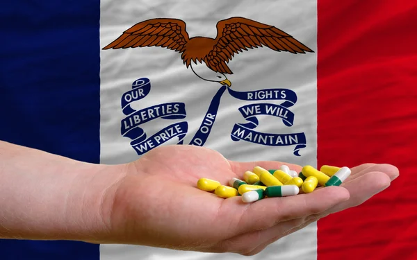 Tenendo le pillole in mano davanti alla bandiera di stato iowa noi — Foto Stock