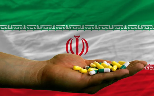 Holding pills in hand in front of iran national flag — Stock Photo, Image