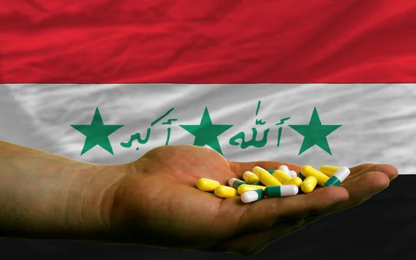 Holding pills in hand in front of iraq national flag — Stock Photo, Image