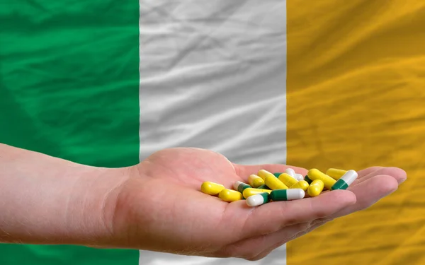 Holding pills in hand in front of ireland national flag — Stock Photo, Image