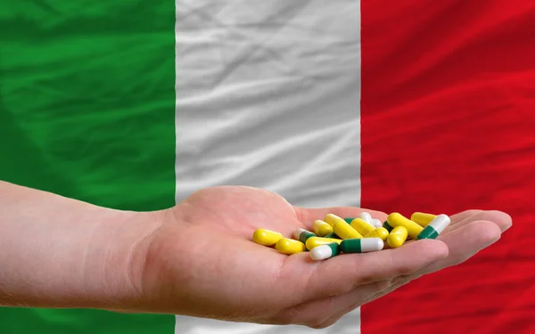 Holding pills in hand in front of italy national flag — Stock Photo, Image