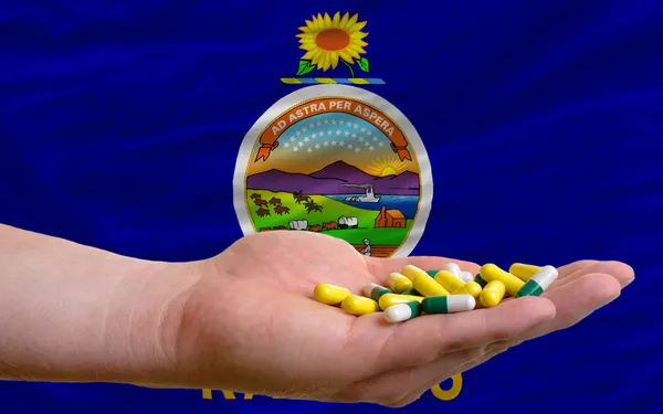 Sosteniendo pastillas en la mano frente a Kansas nos bandera del estado —  Fotos de Stock
