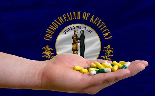 Holding pills in hand in front of kentucky us state flag — Stock Photo, Image