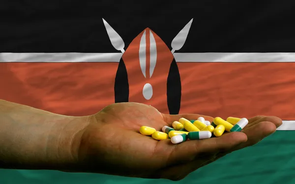 Holding pills in hand in front of kenya national flag — Stock Photo, Image