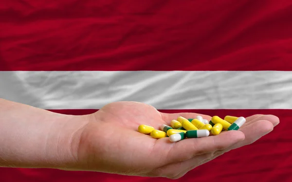 Держа в руках таблетки перед национальным флагом Латвии — стоковое фото