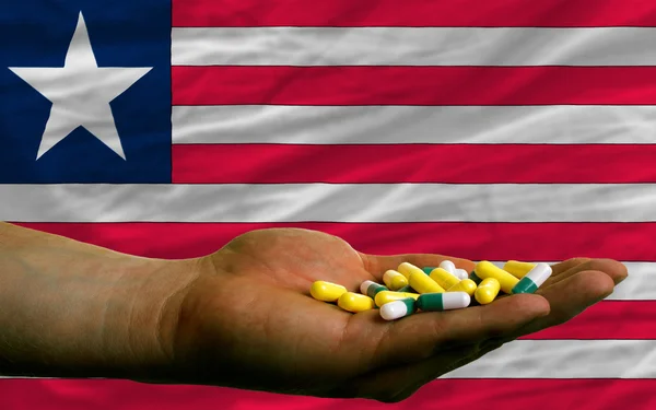 Держа в руках таблетки перед национальным флагом Либерии — стоковое фото
