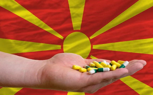 Sosteniendo pastillas en la mano frente a la bandera nacional de macedonia — Foto de Stock