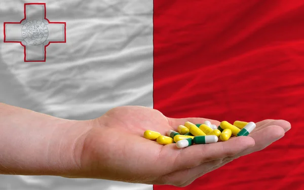 Holding pills in hand in front of malta national flag — Stock Photo, Image