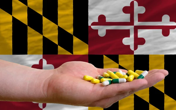 W ręku trzyma tabletki przed maryland nas flaga państwowa — Zdjęcie stockowe