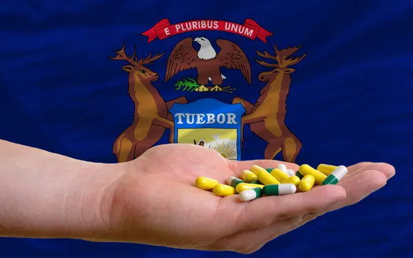 Holding pills in hand in front of michigan us state flag — Stock Photo, Image