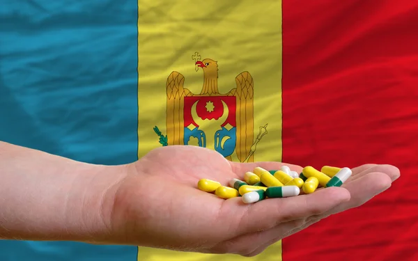 Sosteniendo pastillas en la mano frente a la bandera nacional de Moldavia — Foto de Stock