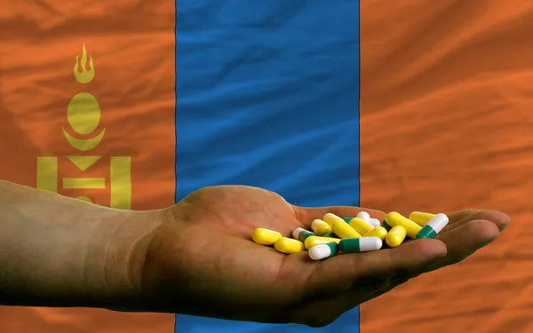 Holding pills in hand in front of mongolia national flag — Stock Photo, Image