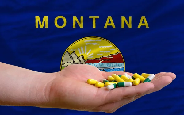 Holding pills in hand in front of montana us state flag — Stock Photo, Image