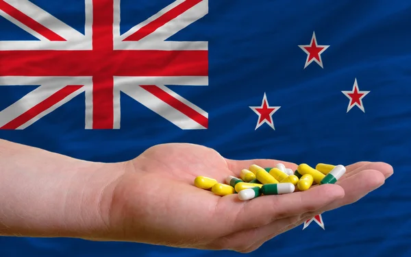 Sosteniendo pastillas en la mano frente a la nueva bandera nacional de Zelanda — Foto de Stock