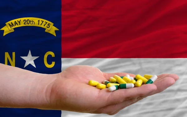 Tenendo le pillole in mano di fronte al nord carolina noi bandiera di stato — Foto Stock