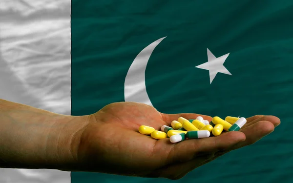 Holding pills in hand in front of pakistan national flag — Stock Photo, Image