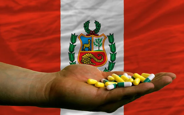 Holding pills in hand in front of peru national flag — Stock Photo, Image