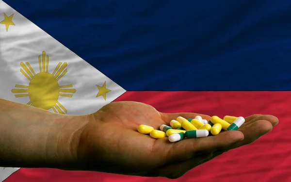 Sosteniendo pastillas en la mano frente a la bandera nacional de Filipinas —  Fotos de Stock