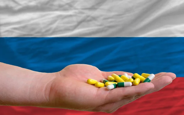 Sosteniendo pastillas en la mano frente a la bandera nacional de Rusia — Foto de Stock