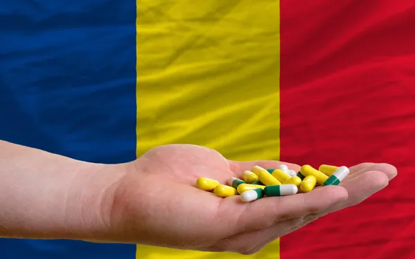 Holding pills in hand in front of romania national flag — Stock Photo, Image