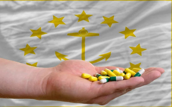 Holding pills in hand in front of rhode island us state flag — Stock Photo, Image