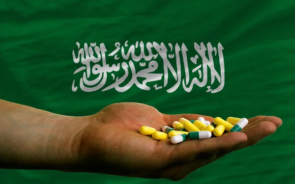 Holding pills in hand in front of saudi arabia national flag — Stock Photo, Image