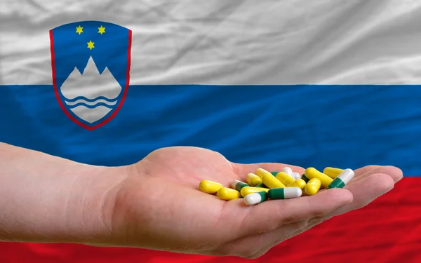 Sosteniendo pastillas en la mano frente a la bandera nacional slovenia — Foto de Stock