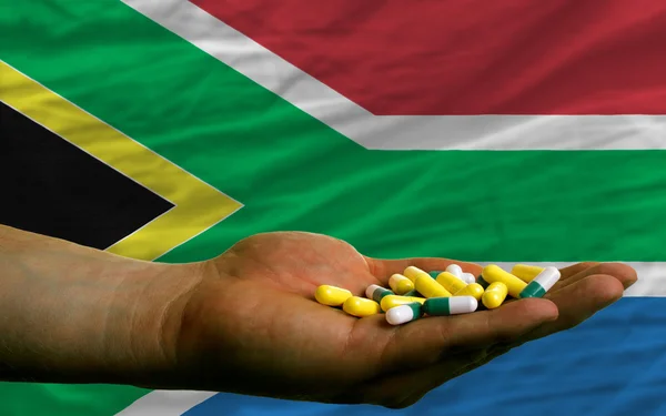 Holding pills in hand in front of south africa national flag — Stock Photo, Image