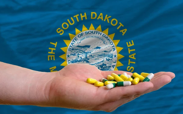 Sosteniendo píldoras en la mano frente a la bandera del estado del sur dakota nosotros —  Fotos de Stock