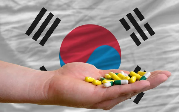 Holding pills in hand in front of south korea national flag — Stock Photo, Image