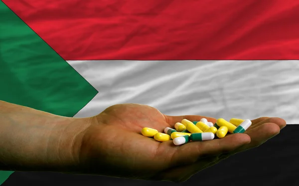 Holding pills in hand in front of sudan national flag — Stock Photo, Image