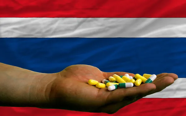 Segurando pílulas na mão na frente da bandeira nacional tailandesa — Fotografia de Stock