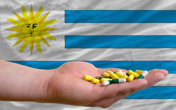 Holding pills in hand in front of uruguay national flag — Stock Photo, Image