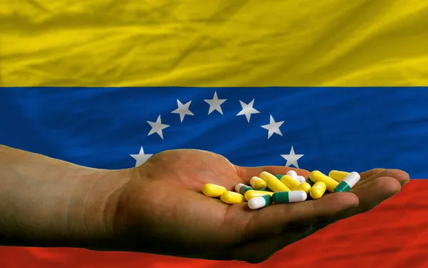 Holding pills in hand in front of venezuela national flag — Stock Photo, Image