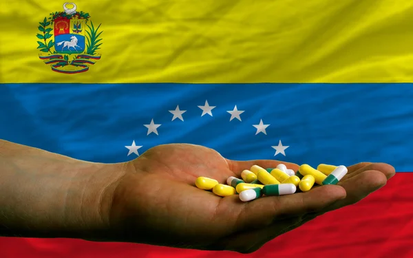 Holding pills in hand in front of venezuela national flag — Stock Photo, Image