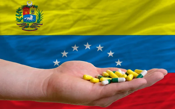 Holding pills in hand in front of venezuela national flag — Stock Photo, Image