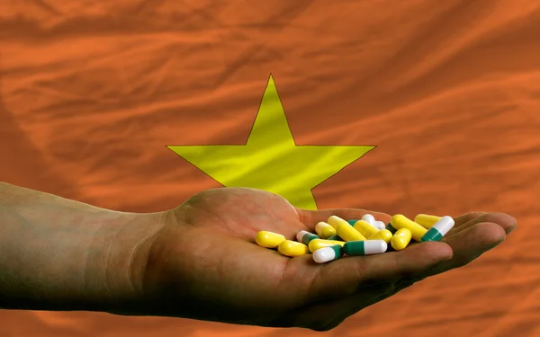 Holding pills in hand in front of vietnam national flag — Stock Photo, Image