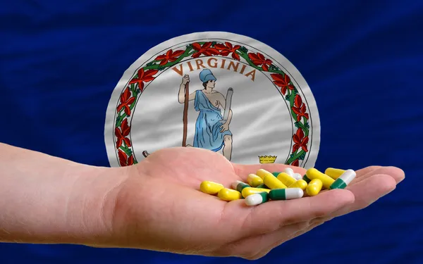 Holding pills in hand in front of virginia us state flag — Stock Photo, Image