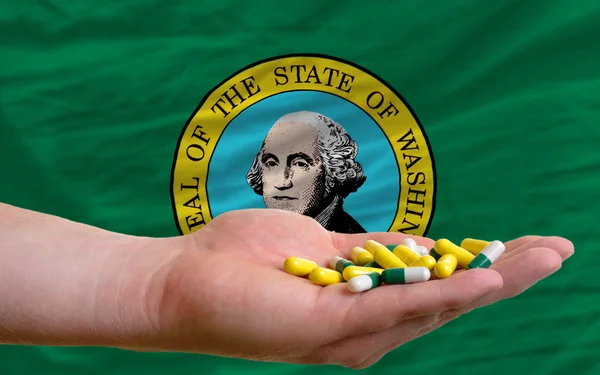 Holding pills in hand in front of washington us state flag — Stock Photo, Image