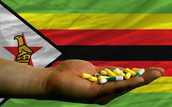 Sosteniendo pastillas en la mano frente a la bandera nacional zimbabwe — Foto de Stock