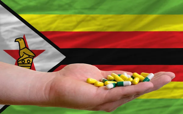 Tabletten in der Hand vor der Nationalflagge Simbabwes — Stockfoto