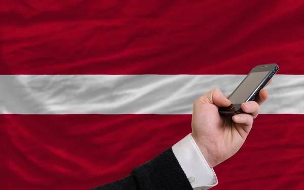 Teléfono celular frente a la bandera nacional de Latvia —  Fotos de Stock