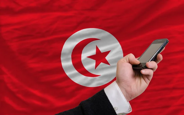 Teléfono celular frente a la bandera nacional de Tunisia — Foto de Stock