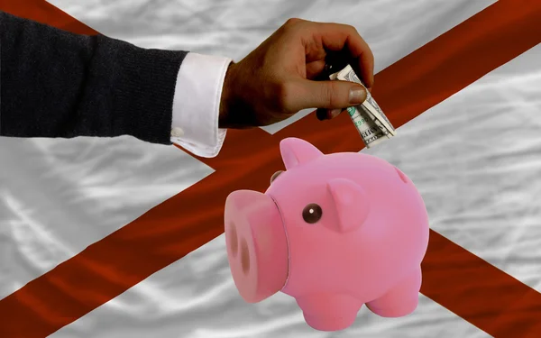 Dólar em porquinho rico banco e bandeira do estado americano de alaba — Fotografia de Stock